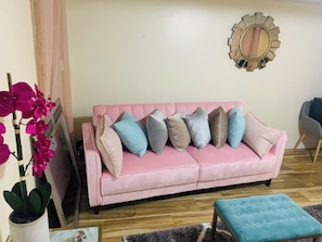 A pink sofa with multiple cushions, a blue ottoman, a mirror, and a potted plant. - STAR PACIFIC- cozy 1 bedroom brooklyn apartment (Brooklyn)