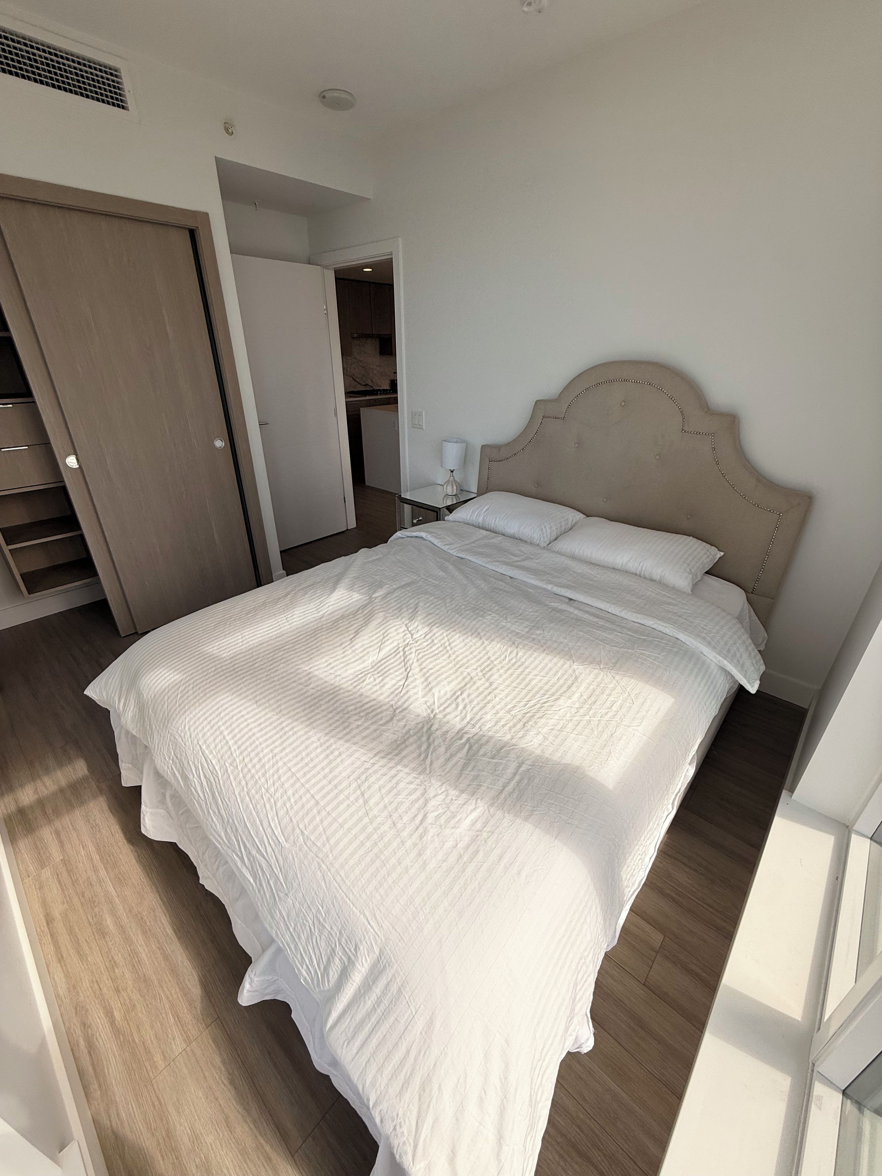 Een slaapkamer met een groot bed, een garderobe en een klein tafeltje met een lamp.