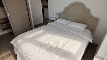 Een slaapkamer met een groot bed, een garderobe en een klein tafeltje met een lamp.