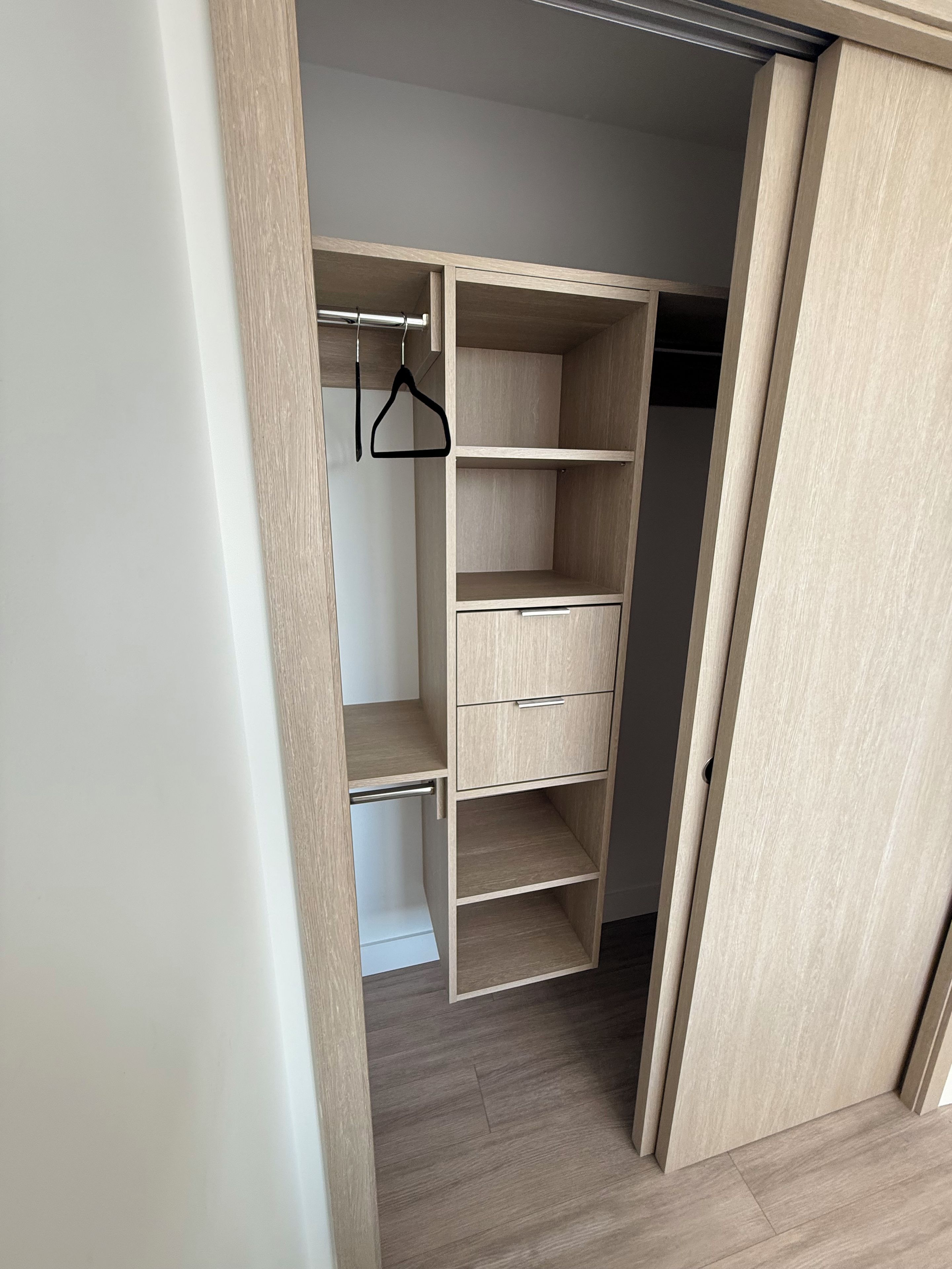 A walk-in closet with open doors, featuring multiple shelves and drawers, and a hanging rod.