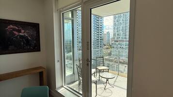 A room with a dining table, chairs, a painting on the wall, and a view of high-rise buildings through large glass doors.