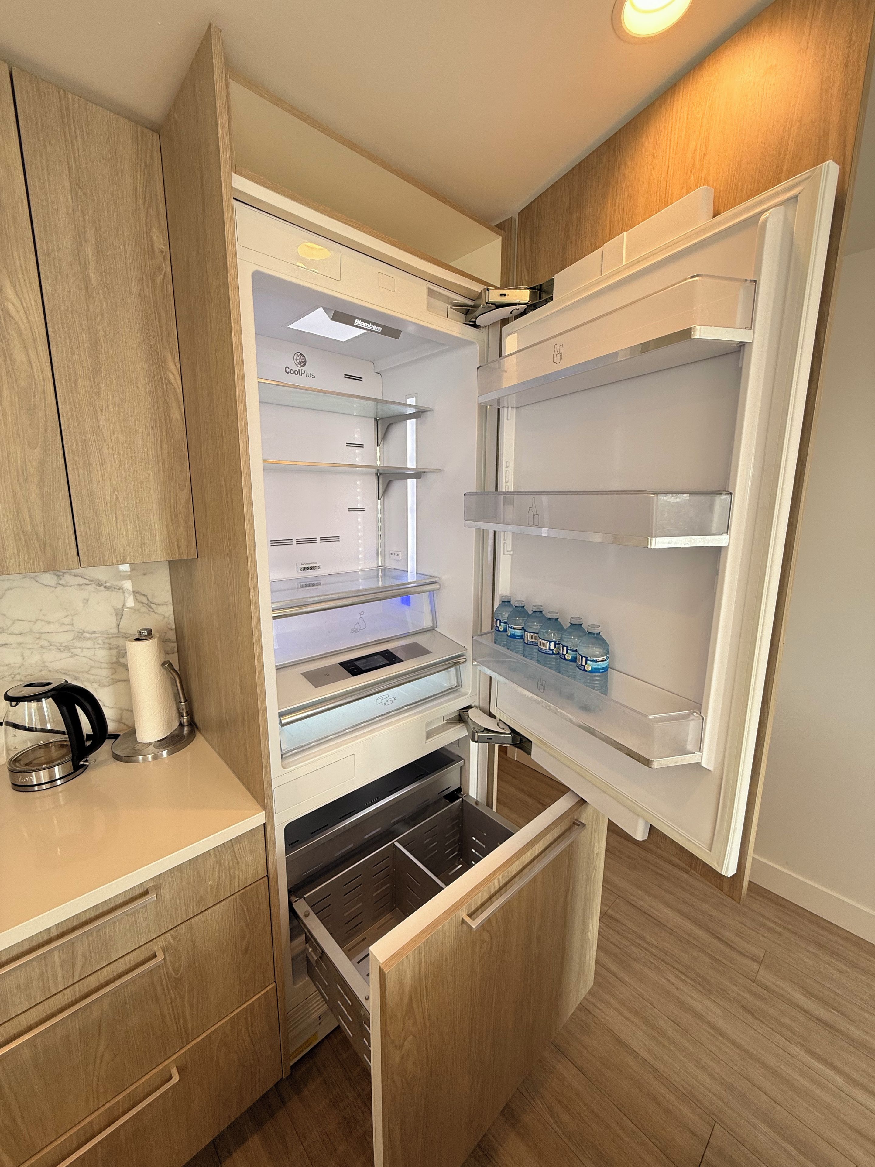 A compact kitchen with a built-in refrigerator, a coffee maker, and a water dispenser on the counter.