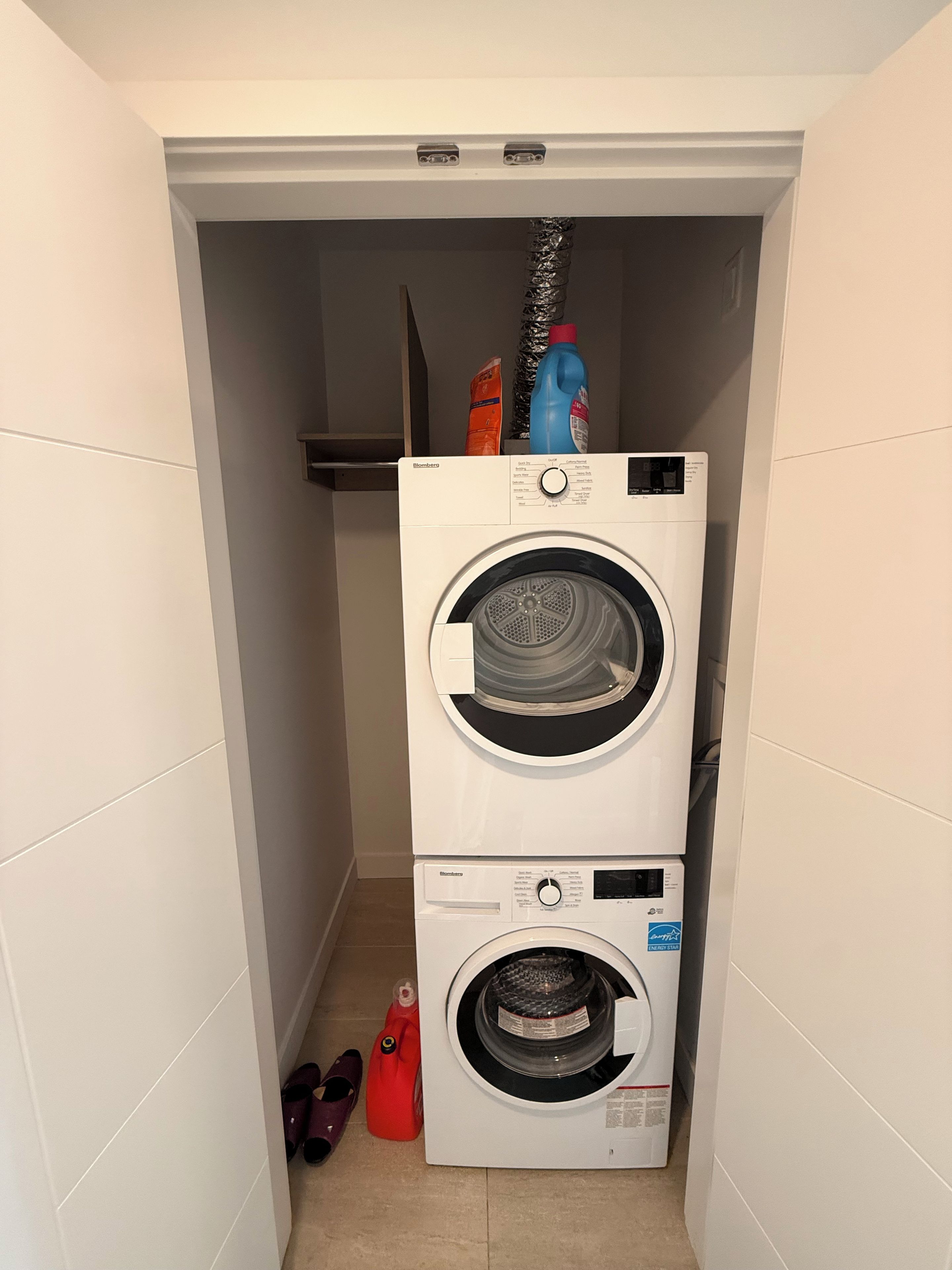 Een wasserette met twee gestapelde wasmachines en een rode schoonmaakfles erboven.