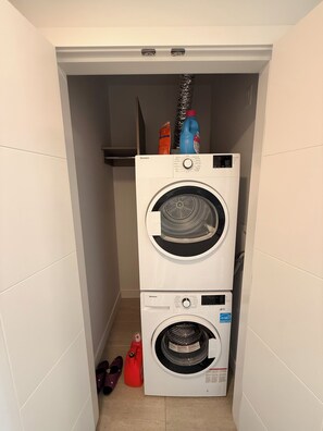 Een wasserette met twee gestapelde wasmachines en een rode schoonmaakfles erboven.