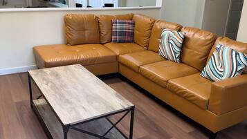 A modern living room with a sectional sofa, a wooden coffee table, and a view of the kitchen through an open space.