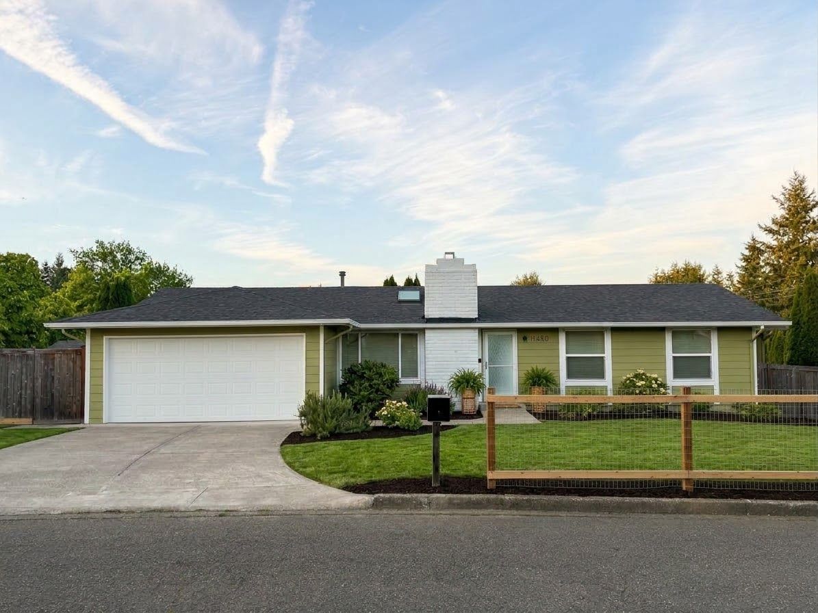 A single-story house with a garage, a fenced yard, and a clear sky.
