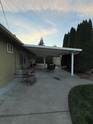 Ein überdachter Patio-Bereich mit Betonboden, einem Tisch und Stühlen sowie einer weißen Pergola.
