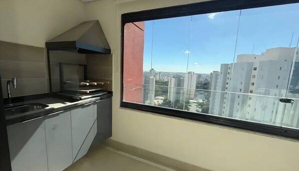 A modern kitchen with a large window, a stove, and cabinets. - Studio in a Sought After Location (Sorocaba)