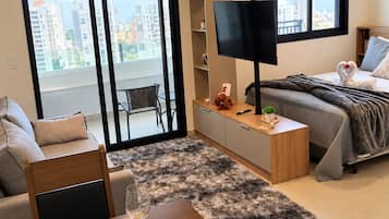 Un apartamento moderno con comedor, cama, televisor y balcón con vista a la ciudad.