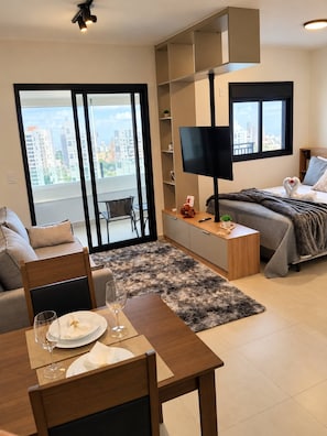 A modern apartment with a dining area, a bed, a TV, and a balcony with a city view. - Studio in a Sought After Location (Sorocaba)