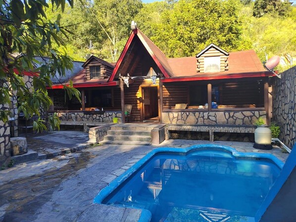 A cabin with a stone exterior, a swimming pool, and a stone staircase leading to the entrance. - New Listing (Santiago)