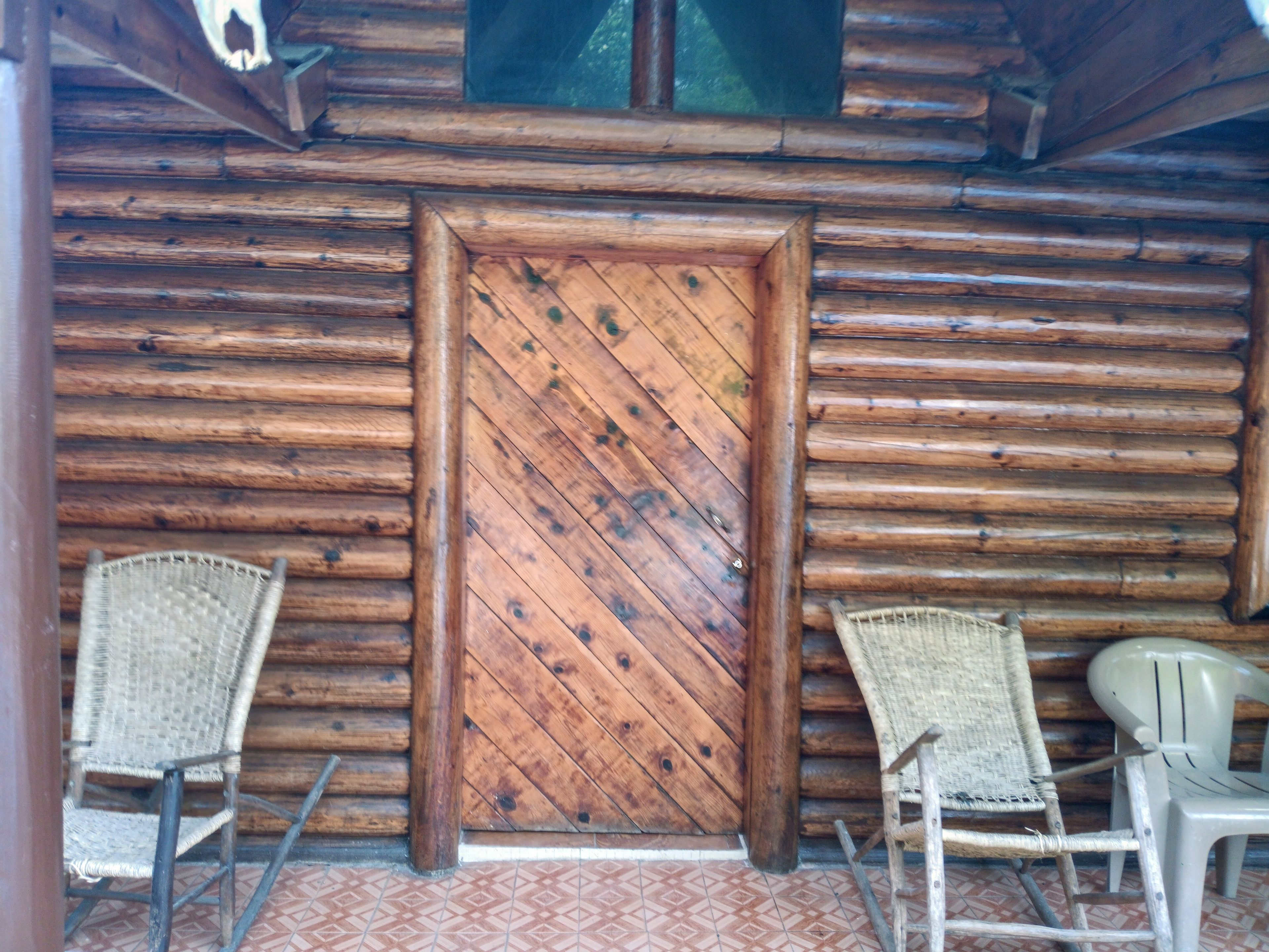 A wooden door with a diamond pattern, flanked by wicker chairs and a plastic chair.