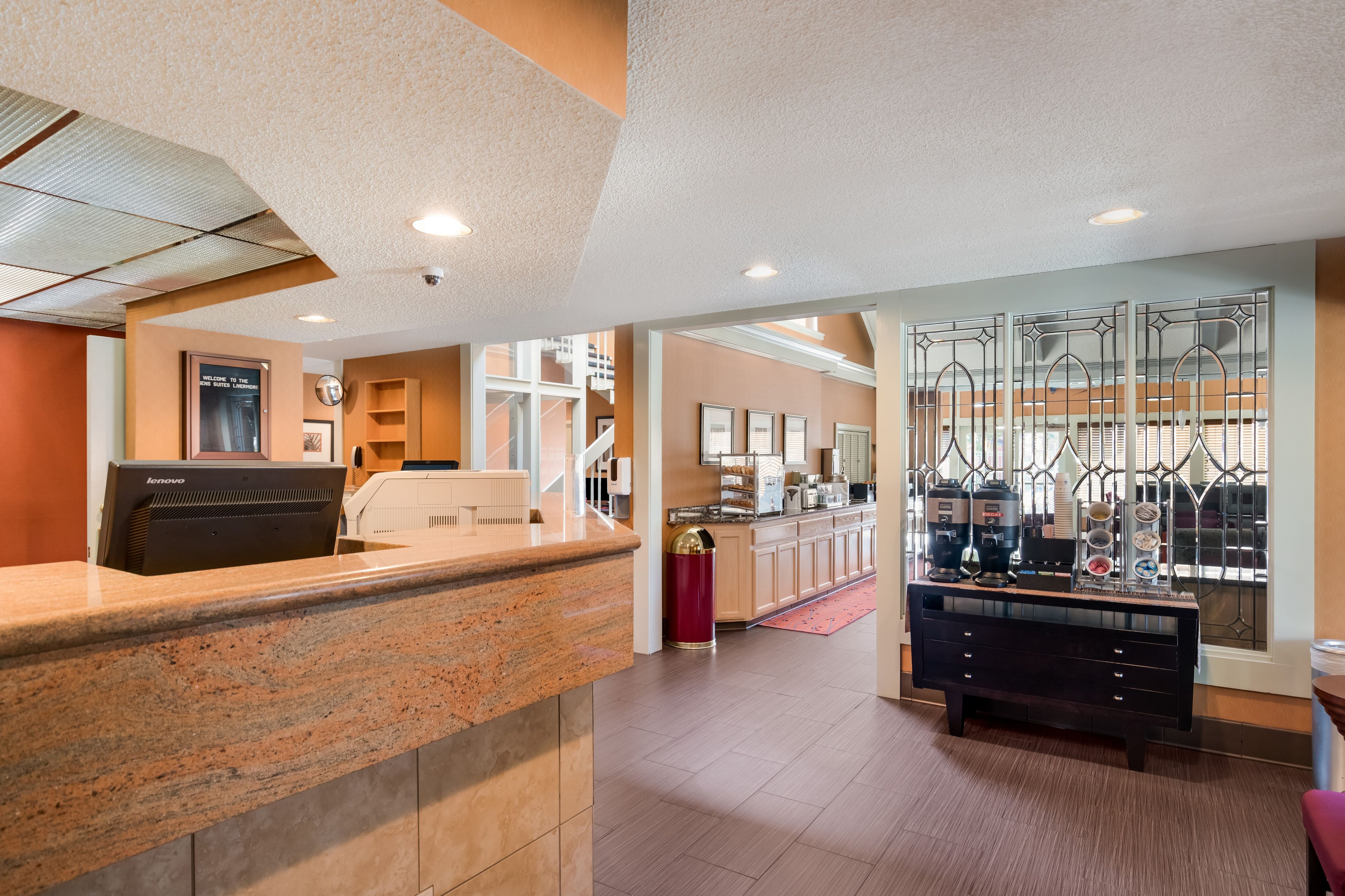A hotel lobby with a reception desk, a coffee station, and a staircase leading to an upper level.