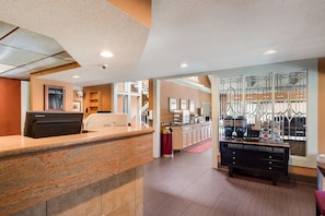 A hotel lobby with a reception desk, a coffee station, and a staircase leading to an upper level. - Su Casa Suites (Livermore)