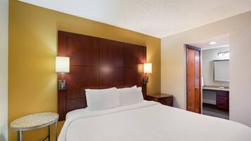A hotel room with a large bed, two bedside lamps, a small round table, and a mirror.
