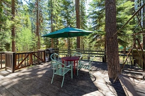 An outdoor deck with a table and chairs, surrounded by trees.