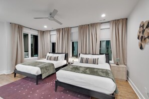 A modern hotel room with two beds, a ceiling fan, and a large window with curtains.