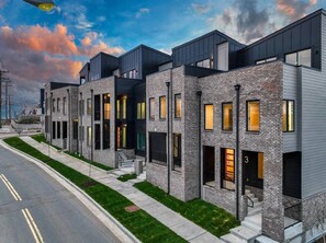 A row of modern townhouses with a uniform architectural style, featuring balconies, large windows, and a well-maintained lawn.