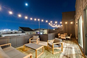 A rooftop terrace with outdoor seating, a bar area, and a city view at night.