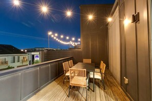An outdoor balcony with a table and chairs, string lights, and a view of the night sky.
