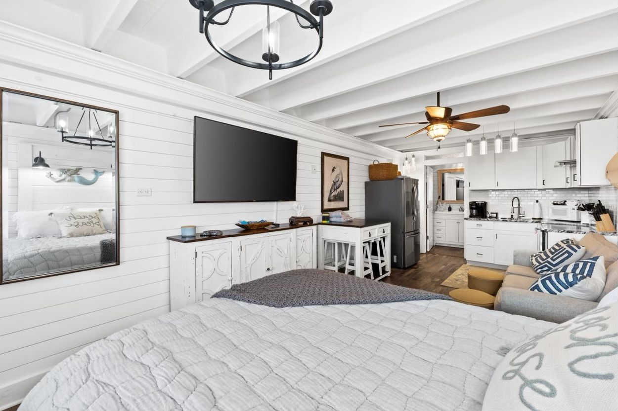 Une chambre moderne avec un grand lit, un téléviseur fixé au mur et, au fond, un coin cuisine.