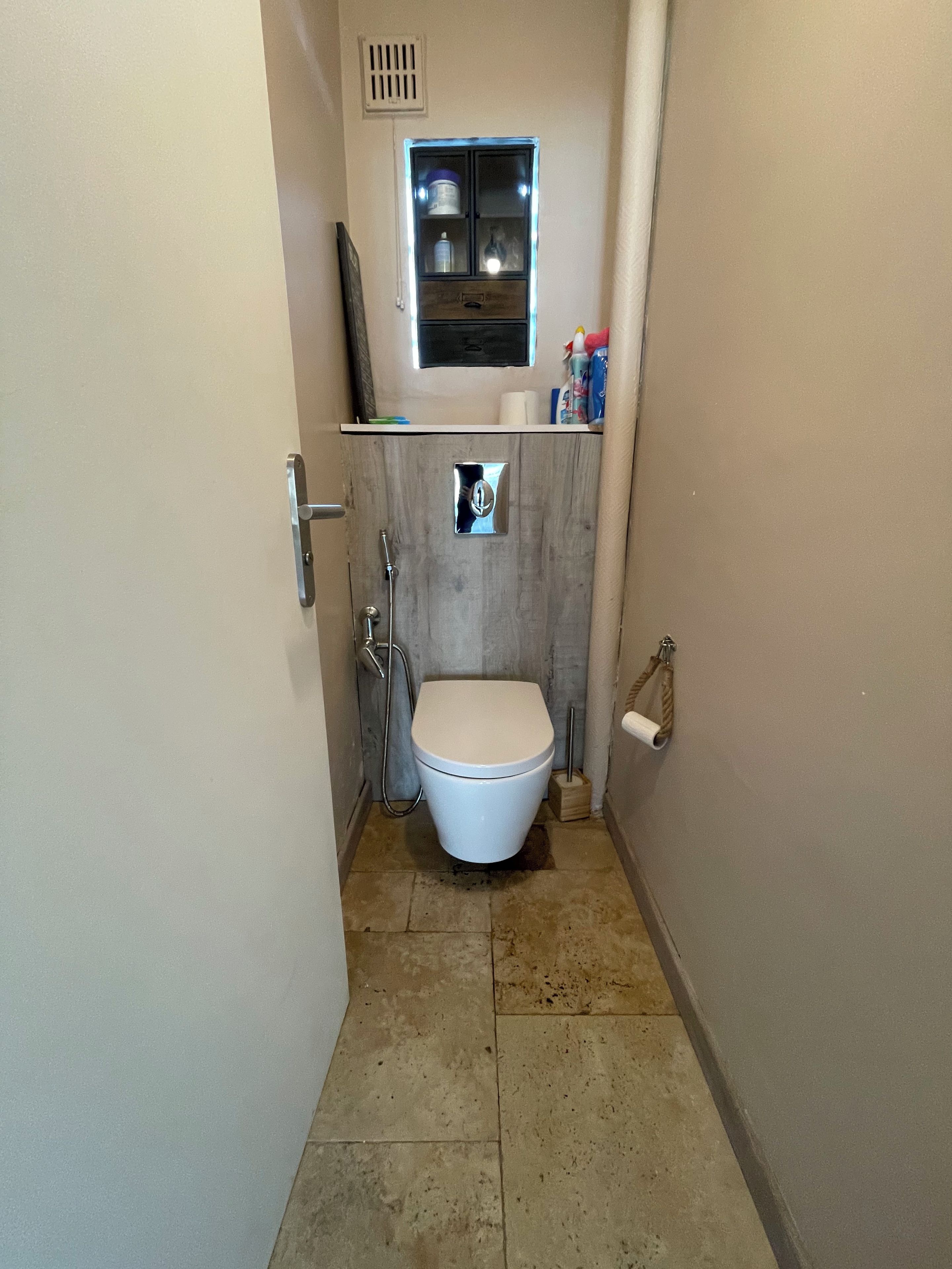 Une petite salle de bain avec des toilettes, une douche et une fenêtre située au-dessus des toilettes.