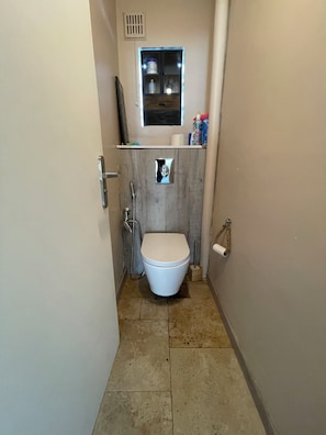 Une petite salle de bain avec des toilettes, une douche et une fenêtre située au-dessus des toilettes.
