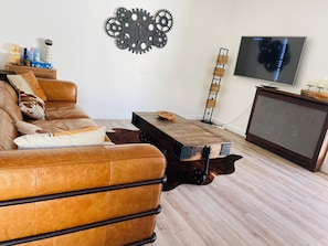 Un salon avec un canapé en cuir marron, une table basse en bois, un téléviseur fixé au mur et un élément décoratif en forme d’engrenage accroché au mur.