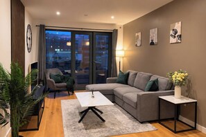 Ein modernes Wohnzimmer mit einem grauen Sofa, einem Couchtisch, einem Beistelltisch und einer Topfpflanze.