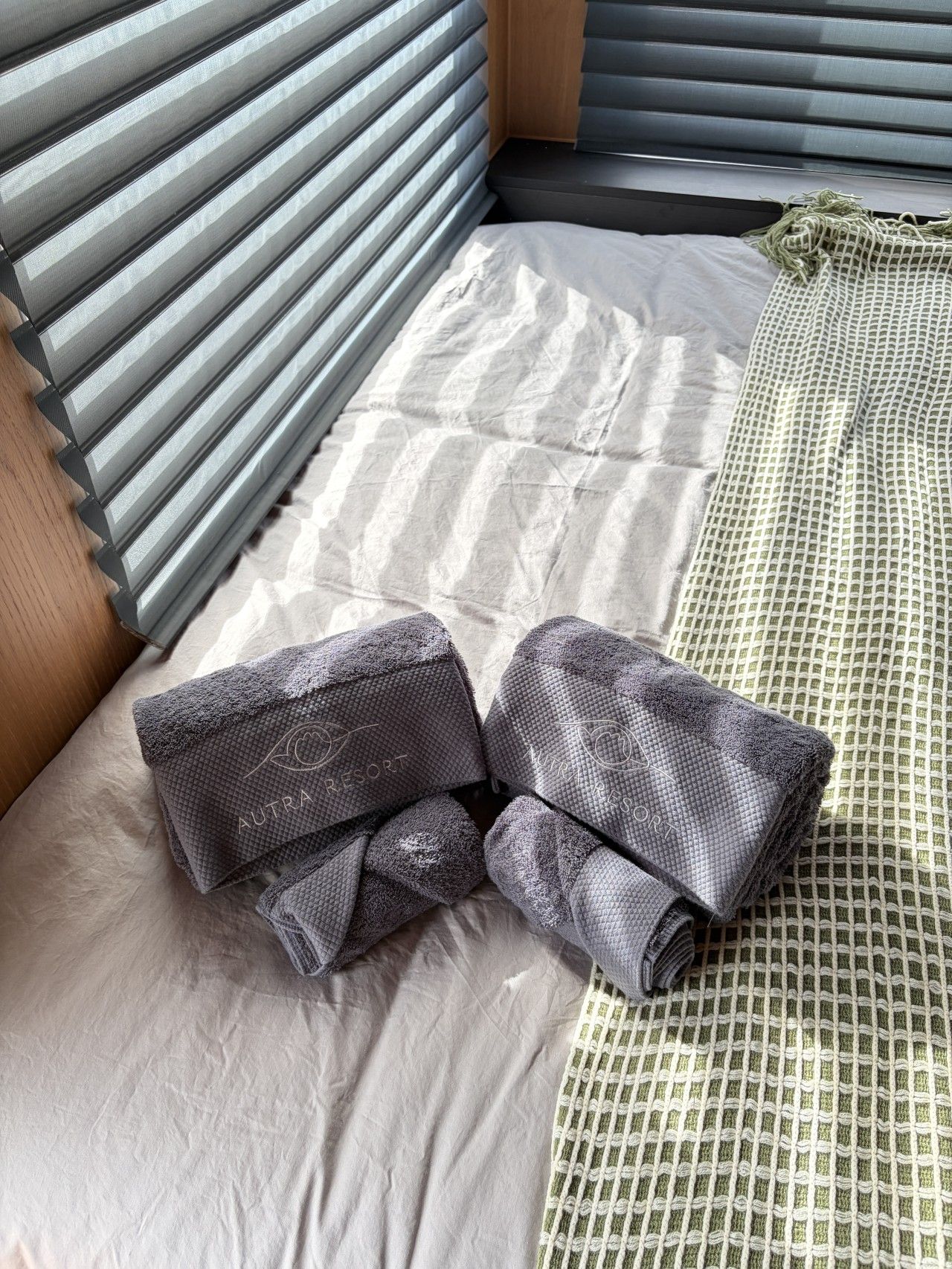 Un lit avec un drap blanc, un oreiller gris et un oreiller à motifs verts.