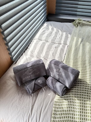 Un lit avec un drap blanc, un oreiller gris et un oreiller à motifs verts.