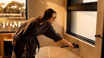 A person in a bathrobe reaching for a bathtub faucet.