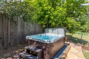Un bain à remous avec une structure extérieure en bois et un banc à l’avant, entouré d’une clôture en bois et d’arbres.
