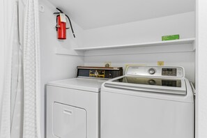 Une buanderie équipée d’un lave-linge et d’un sèche-linge à chargement frontal, d’un extincteur et d’une étagère sur laquelle se trouve une boîte verte.