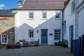 A white building with a blue door and windows, a stone wall, and potted plants. - Bwthyn Gwe Cottage in heart of St Davids (St Davids)