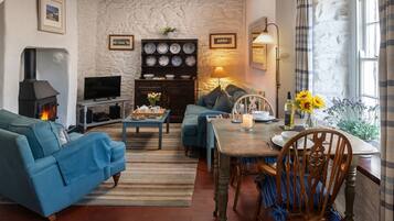 A cozy living room with a fireplace, comfortable seating, a dining table with chairs, and a stone wall.