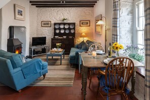 A cozy living room with a fireplace, comfortable seating, a dining table with chairs, and a stone wall. - Bwthyn Gwe Cottage in heart of St Davids (St Davids)