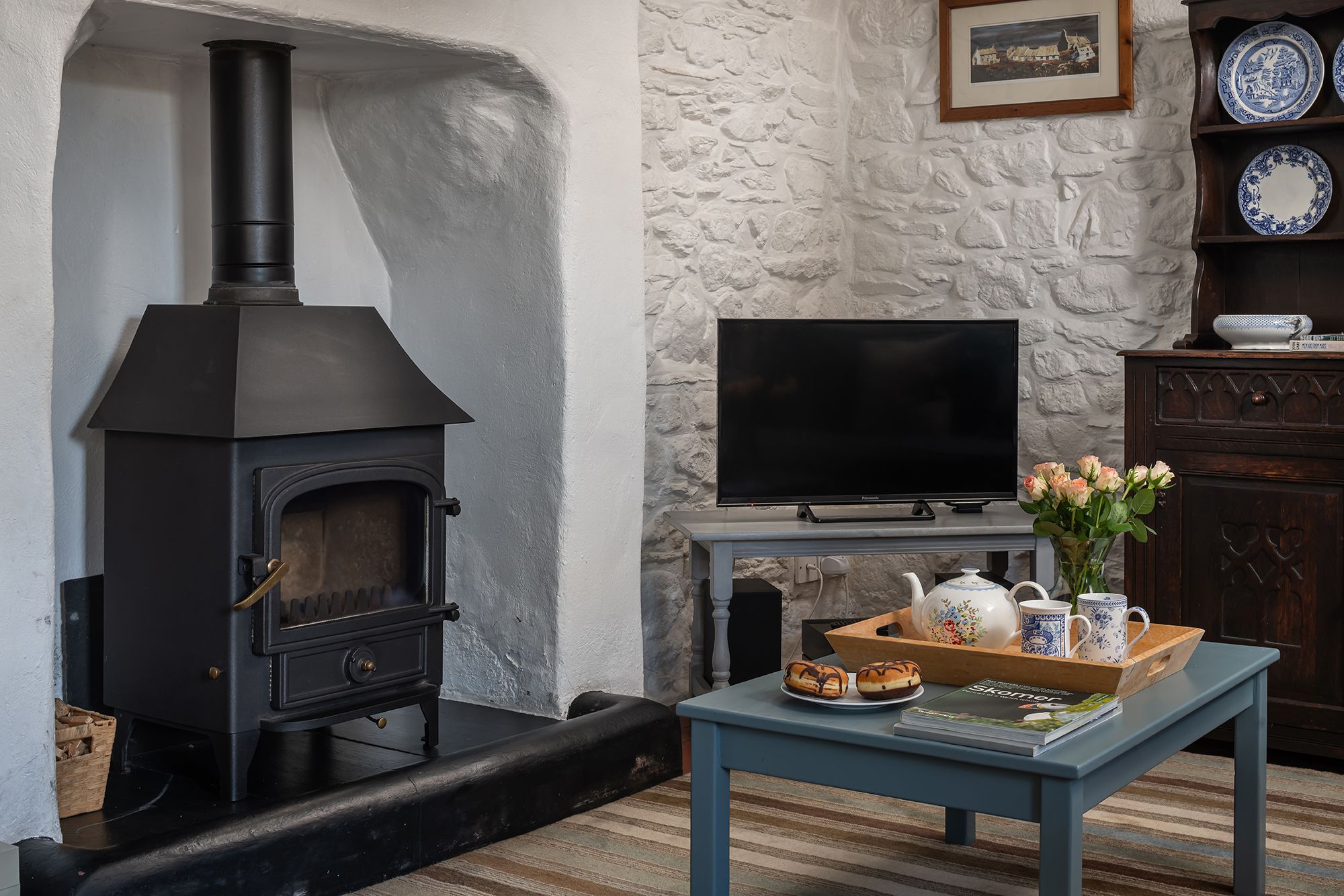 A living room with a black wood-burning stove, a flat-screen TV, and a table with a tray of pastries.