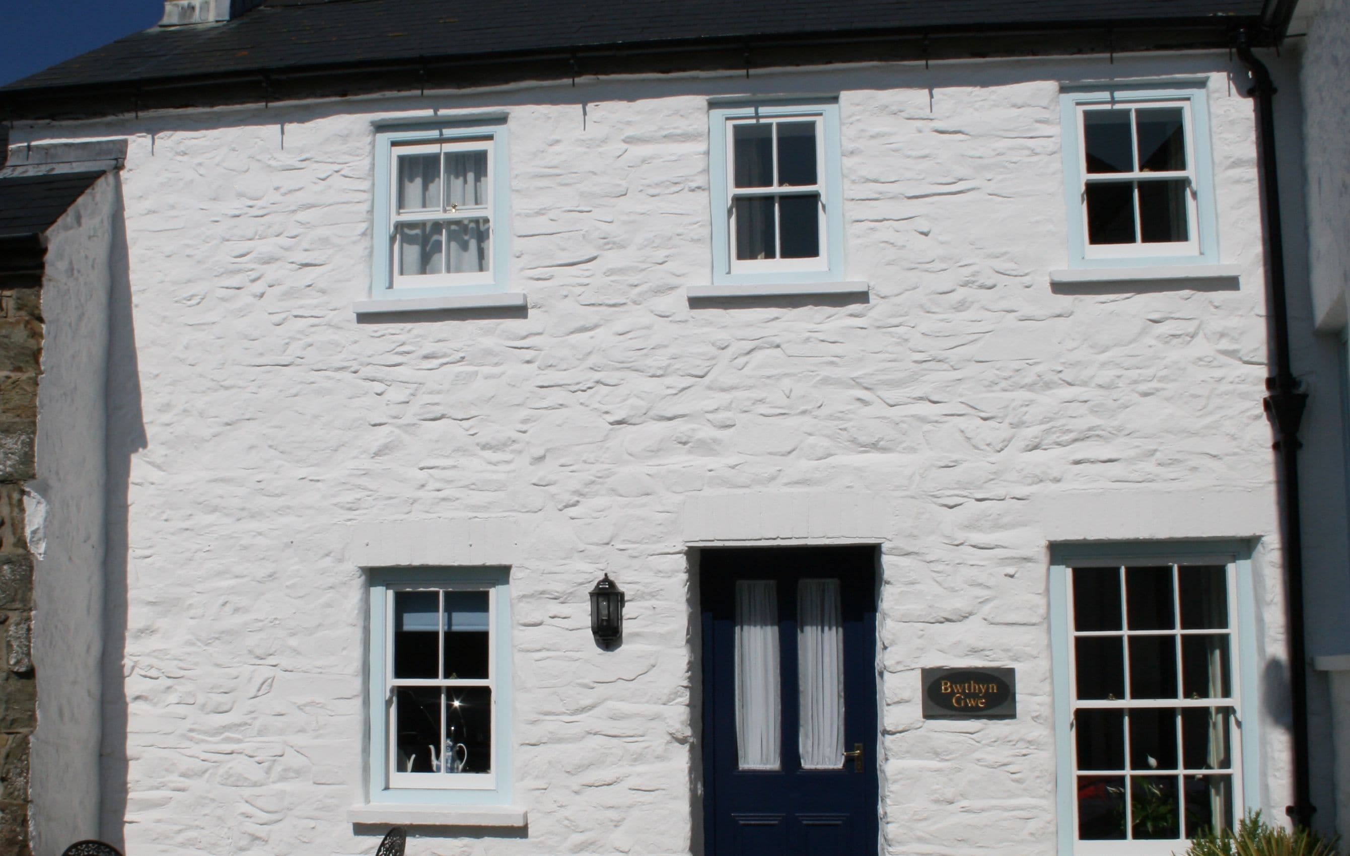 A white building with a blue door, two windows on the upper floor, and a sign reading 'Bwithyn Gwe'.