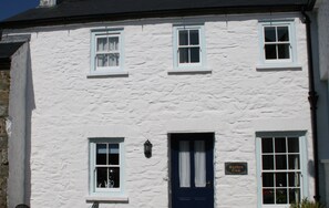 A white building with a blue door, two windows on the upper floor, and a sign reading 'Bwithyn Gwe'. - Bwthyn Gwe Cottage in heart of St Davids (St Davids)