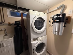 Un espace buanderie comprenant deux machines à laver à chargement frontal, un tuyau d’arrosage et un aspirateur.