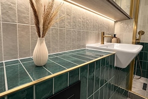 Ein Badezimmer mit einer grünen Marmorarbeitsplatte, einem weißen Waschbecken und einem goldenen Wasserhahn.