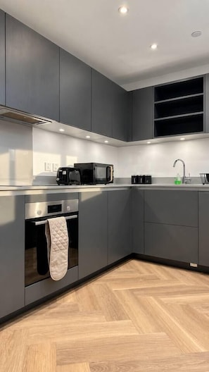 Een moderne keuken met grijze kastjes, een magnetron, een broodrooster en een spoelbak.