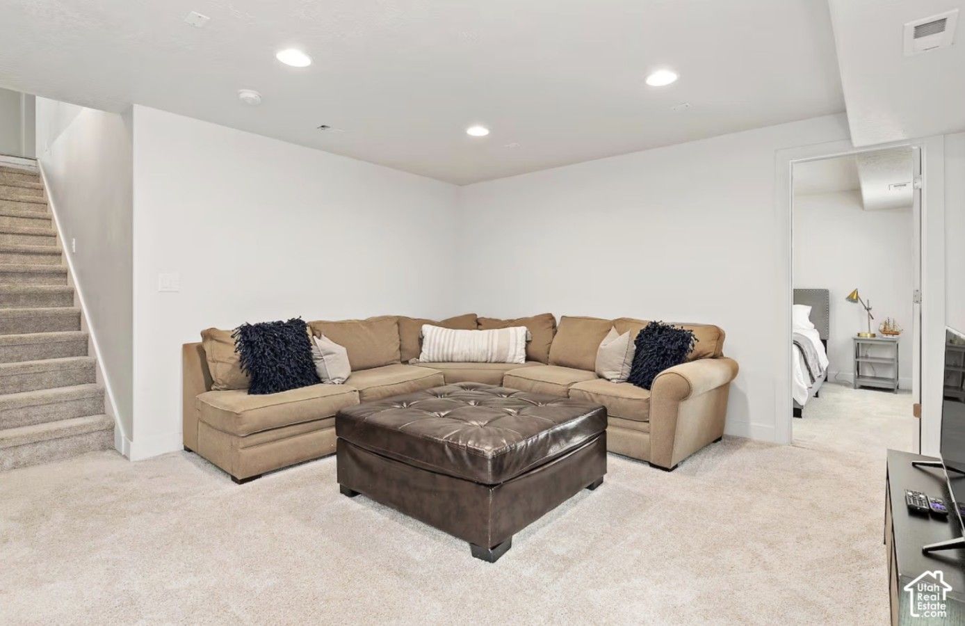 A spacious living room with a sectional sofa, a leather ottoman, and a staircase.