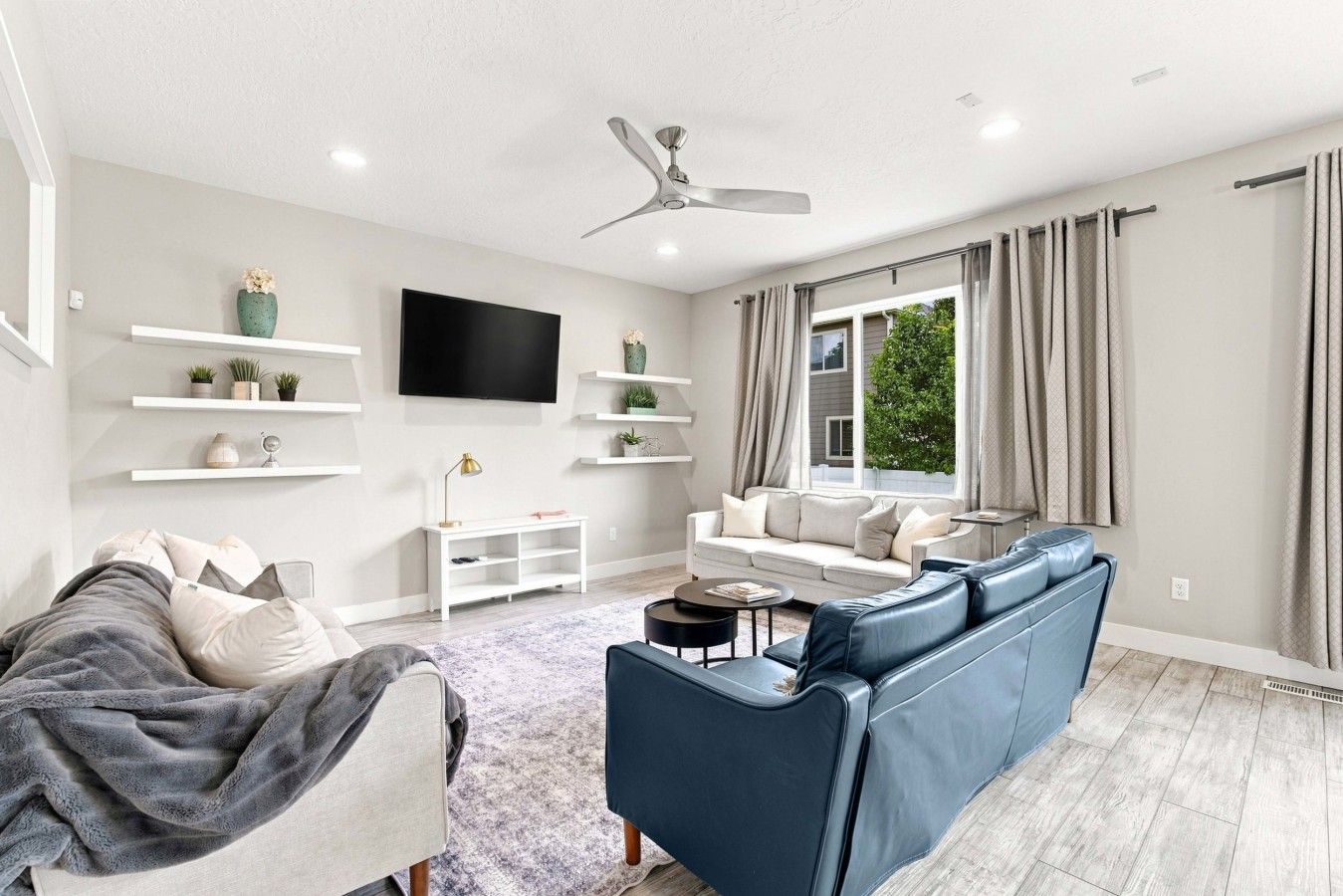 A modern living room with a blue sofa, a white armchair, a flat-screen TV, and a ceiling fan.