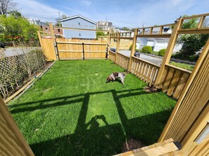 Une cour arrière clôturée avec un chien, une terrasse en bois et une maison en arrière-plan.