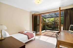 Een hotelkamer met een bed, een bureau en een computer. Er is een schuifdeur naar een buitenruimte met een tuin en een standbeeld.