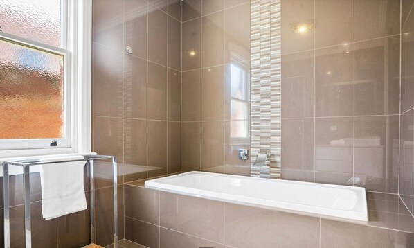 Een moderne badkamer met een douchecabine van glas, een wit bad en een raam met gezandstraald glas.