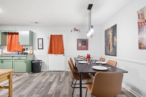 Un comedor con una mesa dispuesta para cuatro, una cocina al fondo y una puerta con cortina naranja.