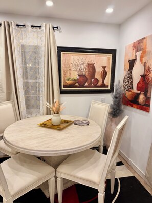 Un comedor con una mesa redonda, sillas, un florero y una obra de arte enmarcada en la pared.